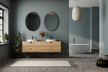 Elegant bathroom with blue tones walls, white basin with oval mirrors, bathtub, shower, plants, and tiled floor. Boho scandinavian bathroom.