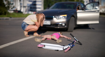 Little girl lies motionless on asphalt with scooter after collision with car.