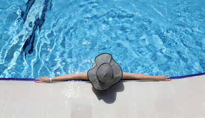 Woman in panama lying on edge of swimming pool top view. Relaxation at resort concept