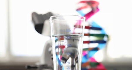 Glass of water standing near dna molecule mockup and microscope in laboratory closeup. Quality control of tap water concept