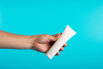 Female hand holds cosmetic product in tube, bottle, lotion or serum on blue background.