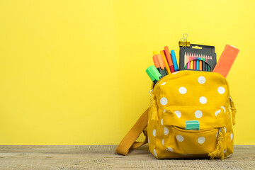 Yellow backpack with white polka dots with different colorful stationery on table. Yellow...