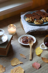 Cup of tea or coffee, plate with desserts, dried oranges, bowl of grapes, scented candles, vintage books, pumpkins and autumn leaves on the table. Autumnal hygge. Selective focus.