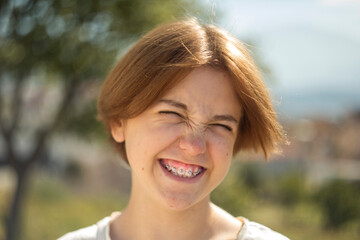 A red-haired teenage girl with braces, sporting a warm smile, radiating youthful charm