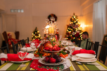 Empty traditional Christmas dinner table inside decorated living room with holiday garlands and dinnerware. Interior of traditional and authentic season cozy setting celebrating religious event.