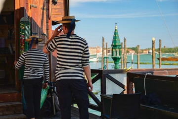 Two gondoliers at the pier of the Venetian Lagoon in Venice, Italy. - obrazy, fototapety, plakaty