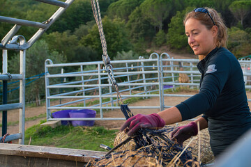 Frau wässert Heu im Netz auf einer Pferdefarm, Bauernhof. Im Hintergrund südliche Landschaft. 