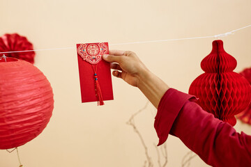 Minimal close up of female hand hanging red envelope on string for good fortune as Chinese New Year...