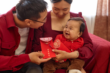 Portrait of happy Asian family with cute baby boy enjoying Chinese New Year celebration at home and...