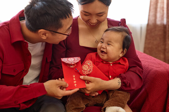 Portrait of happy Asian family with cute baby boy enjoying Chinese New Year celebration at home and holding red envelopes Have overflowing abundance every year