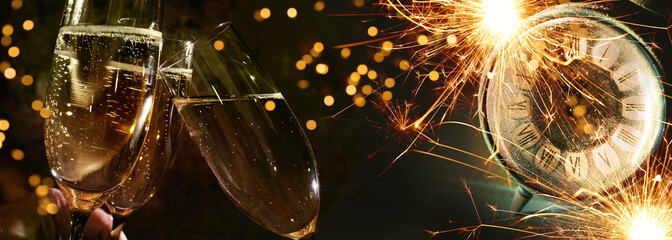Toasting champagne at new year countdown. Glasses of sparkling wine in front of glowing sparklers and alarm clock Horizontal background for New Year's Eve party and invitation. - obrazy, fototapety, plakaty
