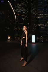 woman with dark hair in elegant dress and accessories walks around the night city with skyscrapers in the background