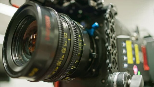 Focus ring of a professional cinema camera turning, focus distance changing. Lens elements and iris ring visible, camera body in background.