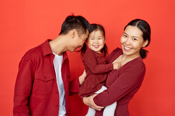 Waist up portrait young young Chinese family holding baby with candid emotions standing against red