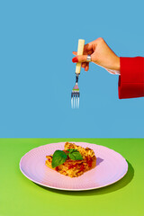Female hand holding fork over delicious Italian food, lasagna over green and blue background....