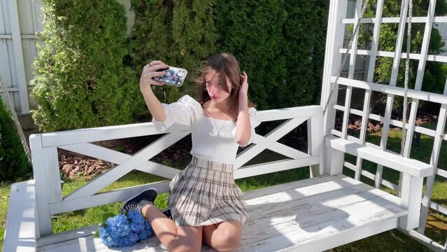 Teen girl making selfie on her phone in the garden on swing