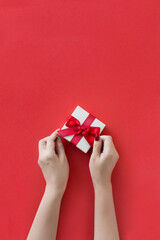 Hand holding a gift box on red background.