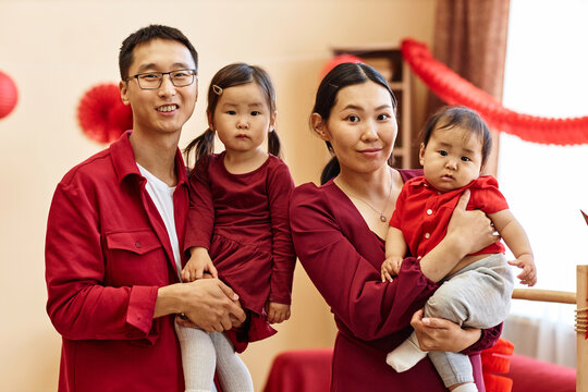 Waist up portrait of happy Chinese family of four looking at camera at home and wearing red together