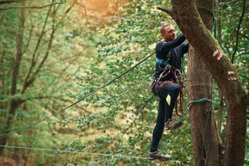 Naklejka na ściany i meble Process of preparing. Man is doing climbing in the forest by use of safety equipment