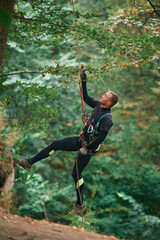 Up on the rope, hanging. Man is doing climbing in the forest by use of safety equipment