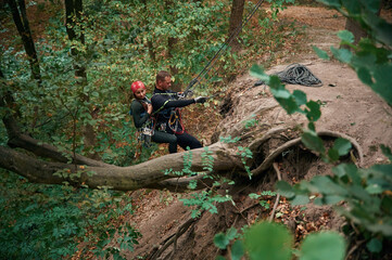 Going down. Man and woman doing climbing in forest with use of safety equipment