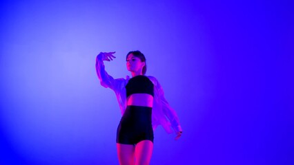 Fototapeta na wymiar Young woman wearing a top, shorts and a shirt performing contemporary dance in studio. Neon blue, pink and red color scheme, ombre, gradient background. Medium sized.