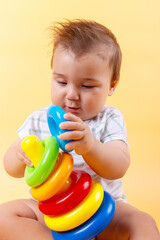 For nine months, the baby plays with a colored pyramid on a yolk background. Emotions, beautiful child.