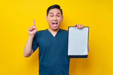 Excited professional young Asian male doctor or nurse wearing a blue uniform holding clipboard with...