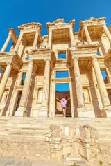 A tourist woman stands in awe before the grandeur of the Library of Celsus in Ephesus, Turkey, her eyes tracing the intricate details of the ancient facade bathed in soft sunlight