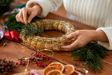 winter holidays, diy and hobby concept - close up of woman with fir branches making christmas wreath at home