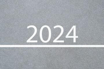 Text 2024 and a white line on light asphalt top view. New Year, beginning concept