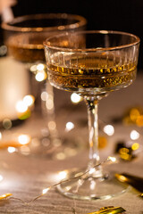 party, celebration and holidays concept - close up of champagne in glasses, electric garland lights and golden confetti on table over black background