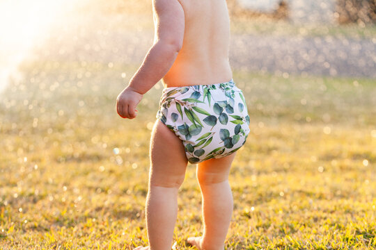 Aussie kid in cloth nappy playing in sprinkler water on a summer afternoon