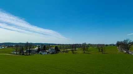 Fototapeta na wymiar An Aerial View of Countryside, with Farms, Green Crops, Trees, Borders, Barns and Silos. on a Sunny Spring Day