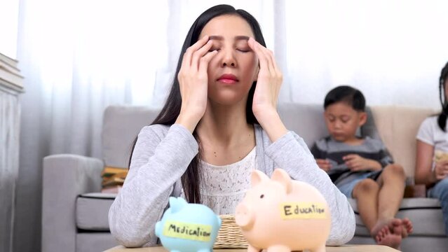 Asian stressful woman or single mom worried about financial planning for education and medication for children and family insurance expenses, mother get headache with empty piggy bank sitting on floor
