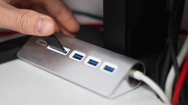 A man inserts an sd card into a card reader and saves photos to a PC. Close-up of hands and slow motion.