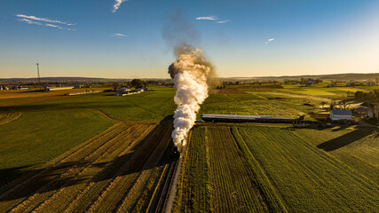 An Aerial View at Sunrise of a Steam Passenger Train Approaching Blowing A Lot of Smoke on a Autumn Day