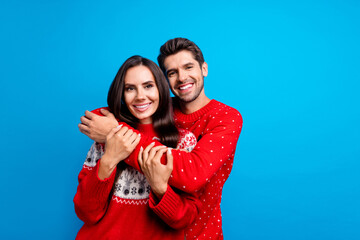 Photo portrait of lovely young spouses hugging cuddle each other dressed x-mas ornament red sweaters isolated on blue color background