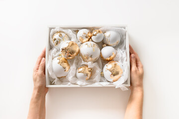 Christmas white balls with gold plated in female hands. Xmas new modern trend for stylish, glamour and luxury decoration. View from above.