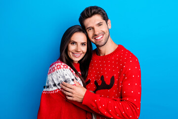 Photo portrait of lovely young spouses hugging care each other dressed x-mas ornament red sweaters isolated on blue color background