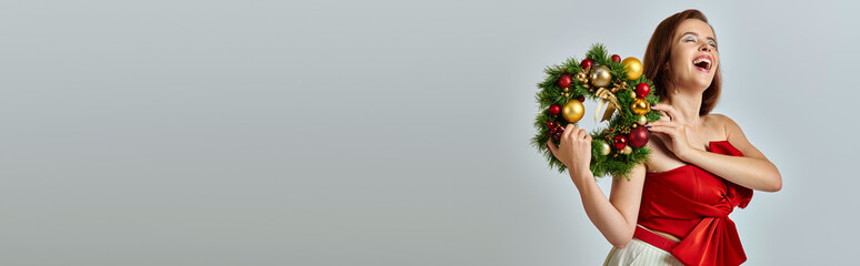 festive season banner, excited woman with shimmery makeup holding Christmas wreath on grey backdrop