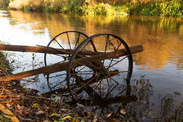 Ecology, environmental conservation. Rusty metal in the water of a quiet small river. Autumn, tree branches and fallen leaves. Reflection in water