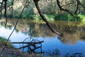 Ecology, environmental conservation. Rusty metal in the water of a quiet small river. Autumn, tree branches and fallen leaves. Reflection in water