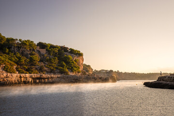 Nebel am Morgen über der Bucht von Cala Llombards zu Sonnenaufgang auf Mallorca