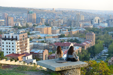 Two girls sit to chat and enjoy the view of Yerevan city in Armenia.
