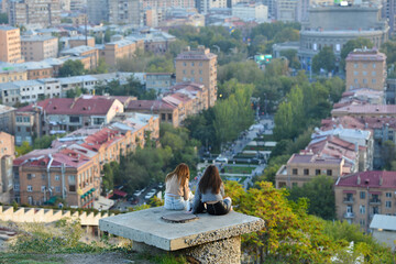 Two girls sit to chat and enjoy the view of Yerevan city in Armenia.