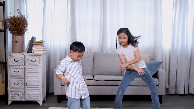 Cute sibling children overjoyed dancing together with cheerful laughing in living room, healthy preschool brother and elder sister playtime enjoy exercise activities funny songs health care lifestyle