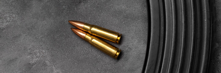 Two bullets for Kalashnikov assault rifle on gray concrete and gradient black background banner....