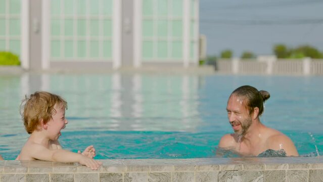 Playful Family Spending Leisure Time Swimming Pool. Cheerful Dad Emerging From The Water Of A Swimming Pool Playing With Cute Kid Son Laughing.