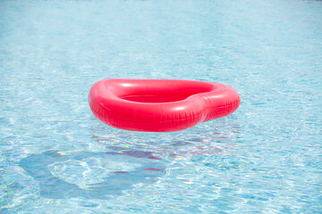Red inflatable ring floating in the swimming blue pool water on summer day
